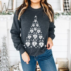 Puede incluir: Una sudadera gris oscuro con un dise&ntilde;o de &aacute;rbol de Navidad blanco formado por caras de perros husky. El &aacute;rbol tiene una estrella en la parte superior y est&aacute; rodeado de estrellas blancas.