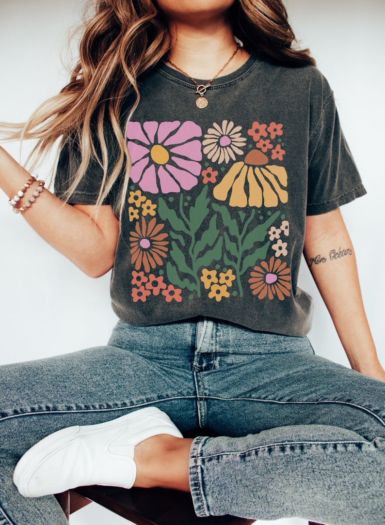 Puede incluir: Una camiseta gris oscuro con un estampado floral colorido. El estampado presenta flores rosas, naranjas, amarillas y verdes.