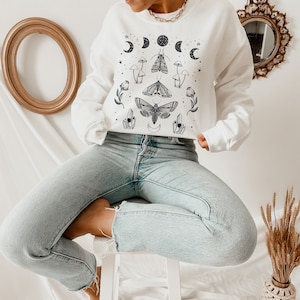 May include: White sweatshirt with a black and white graphic print of moths, mushrooms, and crescent moons.