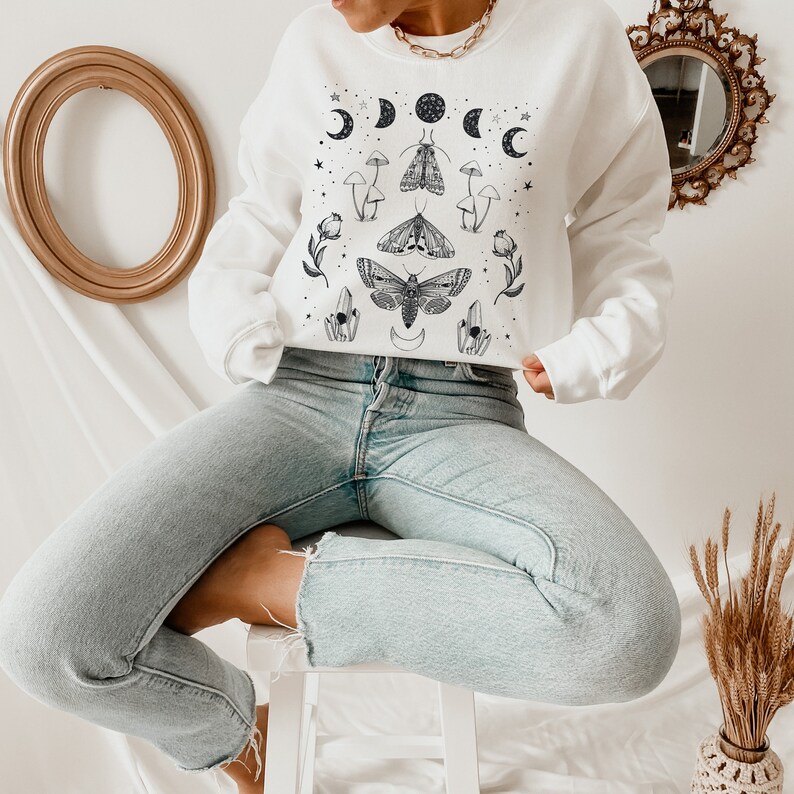 May include: White sweatshirt with a black and white graphic print of moths, mushrooms, and crescent moons.