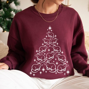 May include: A maroon sweatshirt with a white design of a Christmas tree made of rats. The rats are arranged in a pyramid shape, with the largest rat at the top and the smallest rats at the bottom.