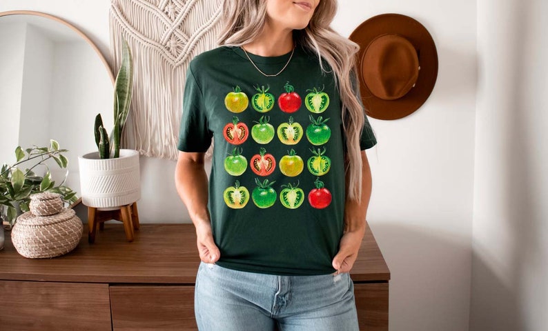 May include: A dark green t-shirt with a graphic print of a grid of tomatoes in various stages of ripeness, from green to red.