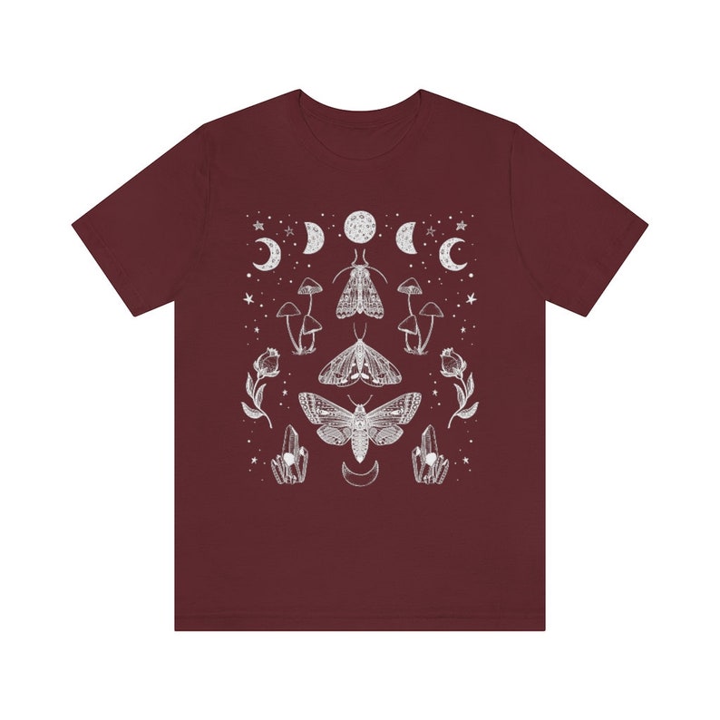Puede incluir: Una camiseta color granate con un dise&ntilde;o gr&aacute;fico blanco que presenta polillas, setas y lunas. El dise&ntilde;o est&aacute; centrado en la camiseta y tiene un patr&oacute;n sim&eacute;trico.