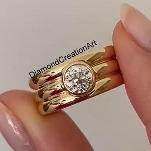 Op de afbeelding: Een gouden ring met drie banden en een grote, ronde, heldere edelsteen in het midden.