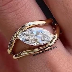 Könnte beinhalten: Ein goldener Ring mit einem Diamanten im Marquiseschliff. Der Diamant ist in einem offenen Band gefasst. Der Ring wird an einem Finger getragen. Der Text "DiamondCreationArt" ist auf dem Ring sichtbar.