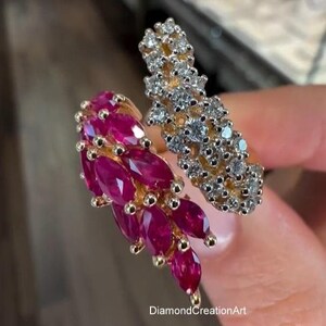 Puede incluir: Un anillo bypass con banda de oro, un lado engastado con rubíes de color rosa intenso en talla marquesa y el otro lado con diamantes blancos en talla brillante redonda. El texto DiamondCreationArt es visible en la base del engaste.
