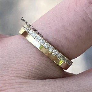 K&ouml;nnte beinhalten: Ein goldener Bandring mit einer Reihe kleiner, klarer Edelsteine am oberen Rand. Der Ring wird auf einem Finger gezeigt, mit dem Text "DiamondCreationArt" sichtbar.