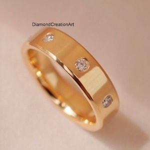 May include: A gold-colored ring with three small, round, clear gemstones set into the band. The ring has a smooth, polished surface and a classic design. The text "DiamondCreationArt" is visible.