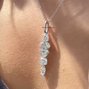 Puede incluir: Un collar de cadena de plata con un colgante que presenta una cascada de diamantes transparentes de diferentes tamaños. El colgante tiene forma de lágrima y los diamantes están engastados en un engaste de garras.