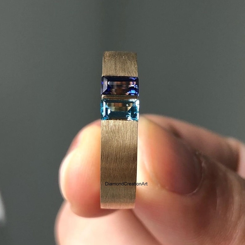 K&ouml;nnte beinhalten: Ein Goldring mit zwei rechteckigen Edelsteinen. Der obere Edelstein ist ein dunkelblauer Saphir und der untere Edelstein ist ein hellblauer Topas.