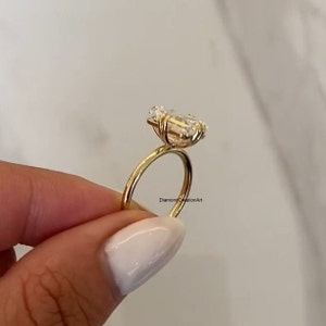 May include: A gold ring featuring a large, clear emerald-cut diamond. The ring is set on a thin band and the diamond is held in place by four prongs. The ring is being held by a hand.