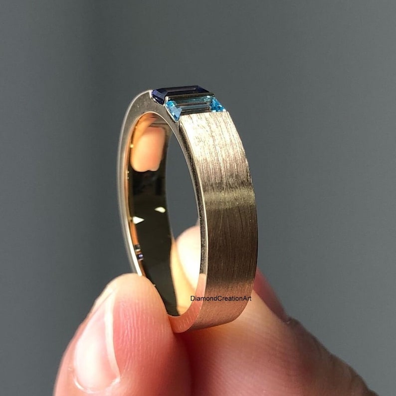 K&ouml;nnte beinhalten: Ein goldener Ring mit geb&uuml;rsteter Oberfl&auml;che und zwei blauen Edelsteinen, die in die Band eingefasst sind. Der Text "DiamondCreationArt" ist auf der Band sichtbar.