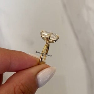 May include: A gold engagement ring featuring a large, clear emerald-cut diamond. The ring is set on a thin band and has a simple, elegant design.