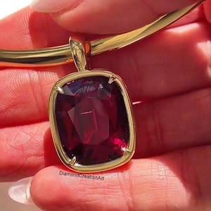 Könnte beinhalten: Eine goldfarbene Halskette mit einem großen, rechteckigen, tiefroten Edelsteinanhänger. Der Anhänger ist in einen goldenen Rahmen gefasst und hat eine facettierte Oberfläche. Der Text "DiamondCreationArt" ist auf dem Anhänger zu sehen.