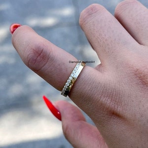 K&ouml;nnte beinhalten: Ein goldener Bandring mit einer Reihe kleiner, klarer Edelsteine an einer Kante. Der Ring wird an einem Finger getragen, mit dem Text "DiamondCreationArt" im Hintergrund.