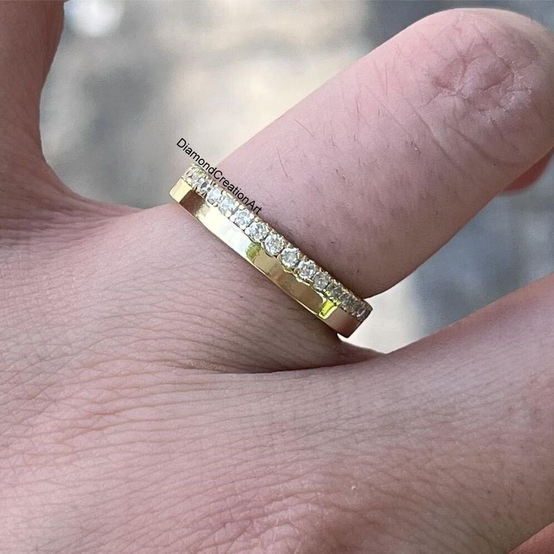 K&ouml;nnte beinhalten: Ein goldener Bandring mit einer Reihe kleiner, klarer Edelsteine am oberen Rand. Der Ring wird auf einem Finger gezeigt, mit dem Text "DiamondCreationArt" sichtbar.