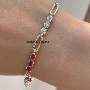 May include: A gold chain link bracelet featuring alternating sections of clear rectangular stones and deep red square stones. The bracelet has a repeating pattern of elongated gold links connected to clusters of three gemstones. The text DiamondCreationArt is visible.