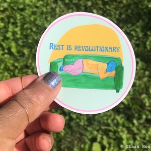 May include: Round sticker with the text "REST IS REVOLUTIONARY" above an illustration of a person resting on a green couch. The person is wearing pink pants and an orange shirt. The background is light blue with a yellow sun.