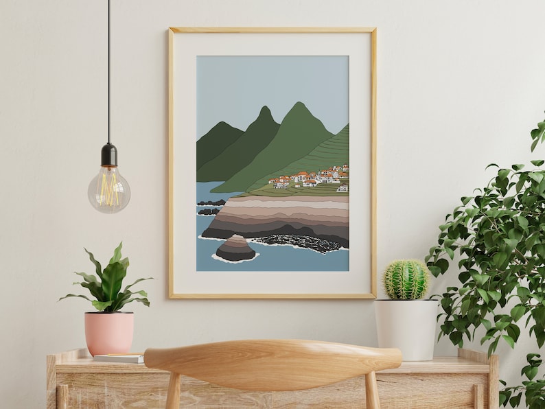 May include: A framed illustration of a coastal landscape with a small village nestled in the hills. The scene features a blue ocean, green hills, and a rocky coastline.