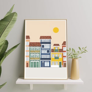 May include: A framed illustration of a row of colorful buildings with a yellow sun in the sky. The buildings are in a variety of colors, including red, yellow, blue, and green. The illustration is on a light beige background.