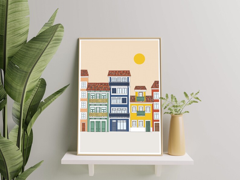 May include: A framed illustration of a row of colorful buildings with a yellow sun in the sky. The buildings are in a variety of colors, including red, yellow, blue, and green. The illustration is on a light beige background.