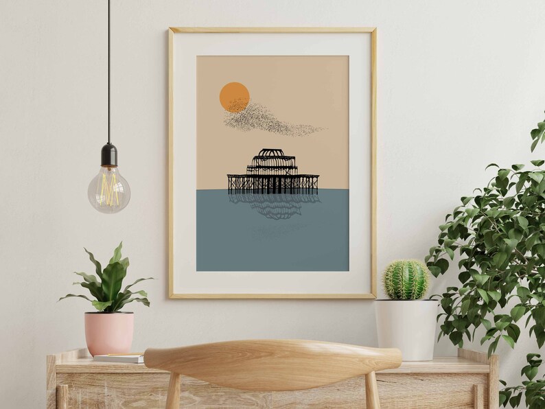 May include: A framed print of a black and white illustration of a pier with a large sun and a flock of birds in the sky. The background is a light brown color with a blue ocean.