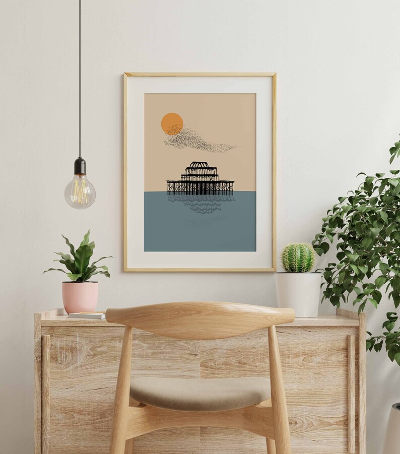 May include: A framed print of a black and white illustration of a pier with a large orange sun in the background. The pier is reflected in the blue water below.