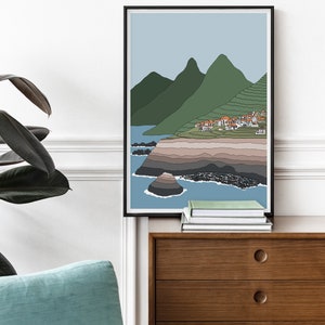 May include: A minimalist line art print of a coastal landscape with green mountains, a small village, and a rocky shoreline. The print is framed in black and has a light blue background.