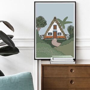 May include: A framed illustration of a white cottage with a thatched roof, surrounded by green foliage and palm trees. The cottage has a brown door and two windows with blue frames.