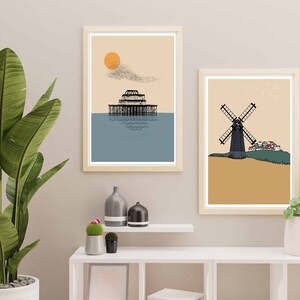 May include: Two framed illustrations, one depicting a pier with a sun and birds in the sky, the other depicting a windmill with a small village in the background. Both illustrations are in a minimalist style with muted colors.