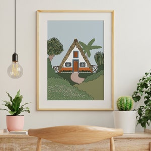 May include: A framed illustration of a white triangular house with a thatched roof, orange door, and green windows. The house is surrounded by green bushes and trees, including a palm tree. The background is a light blue sky.