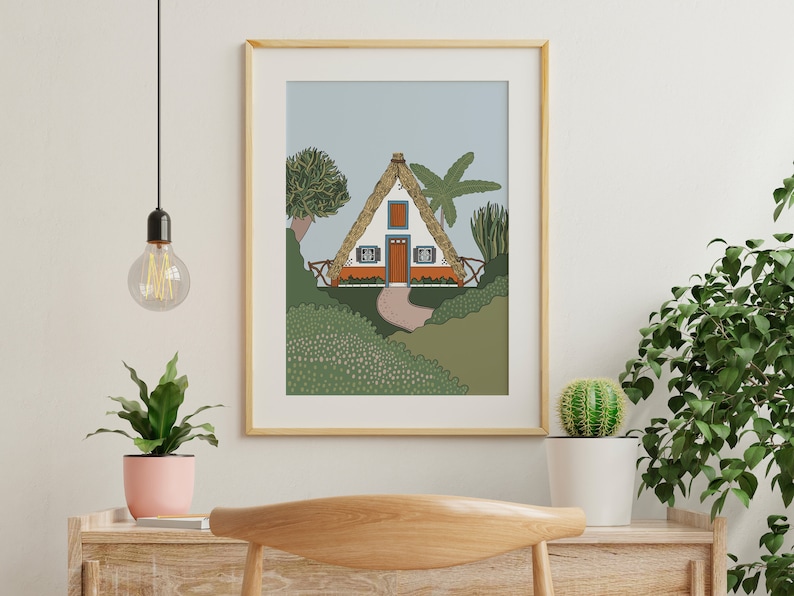 May include: A framed illustration of a white triangular house with a thatched roof, orange door, and green windows. The house is surrounded by green bushes and trees, including a palm tree. The background is a light blue sky.