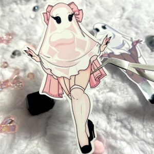 May include: A pink and white ghost sticker with a white sheet and a pink dress. The ghost has black eyes and eyelashes and is wearing a pink bow. The sticker is on a white background.