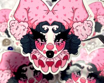 May include: A pink and white sticker with a cartoon clown face. The clown has black hair, pink cheeks, and a red heart-shaped nose. The clown is wearing a pink hat with white polka dots and a white collar with red hearts.