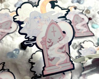 May include: A sticker featuring a ghostly figure with long white hair, a pink dress, and a cross on a tombstone. The figure is surrounded by bats and a crescent moon. The sticker is on a white background.