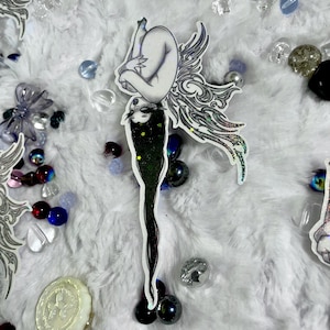 May include: A white ceramic mug with a black handle and the text "But First, Coffee" in a black, handwritten-style font. The mug is on a white surface.