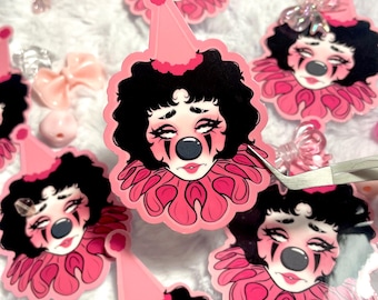 May include: A set of pink and black clown stickers with a sad expression. The stickers feature a clown with black hair, a pink hat, and a pink ruffle collar.