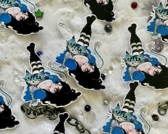 May include: Multiple die-cut stickers featuring an illustration of a character with long black hair and striped stockings, accompanied by a blue cat-like creature. The stickers are scattered among metal safety pins and a metal chain.