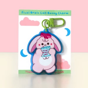May include: Pink bunny charm with blue outline holding a blue and green box that says "Final Brain Cell". The charm is attached to a green metal key ring.