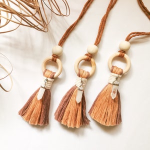 May include: Three brown and beige tassel necklaces with wooden rings and clear crystal charms. The necklaces are hanging against a white background.