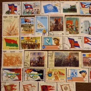 Op de afbeelding: Een verzameling kleurrijke postzegels met vlaggen, historische figuren en herdenkingsontwerpen. De postzegels tonen verschillende landen en evenementen, met tekst en cijfers zichtbaar. De postzegels zijn gerangschikt op een plat oppervlak.