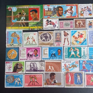 May include: A collection of vintage postage stamps featuring various Olympic boxing scenes, athletes, and international Olympic games themes. The stamps display diverse colors, denominations, and text including Republica de Guinea Ecuatorial, Munich 72, and Montreal 76, arranged in a grid pattern.