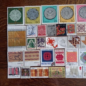Op de afbeelding: Een verzameling van diverse postzegels met uiteenlopende ontwerpen, waaronder kantpatronen, traditionele kunst, geometrische vormen en culturele motieven uit landen als Hongarije, Indonesië, de VS, Venezuela en Australië, gerangschikt in een raster.