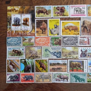 Könnte beinhalten: Eine Sammlung von Briefmarken mit verschiedenen Abbildungen von Elefanten und Nashörnern. Die Briefmarken zeigen unterschiedliche Farben, Nennwerte und Ländernamen wie Malawi, Nicaragua, Adschman, Sambia, Laos und Tansania, die in einem Raster angeordnet sind.