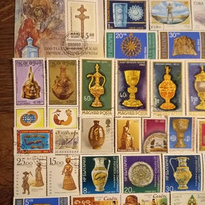 Op de afbeelding: Een verzameling kleurrijke postzegels met diverse ontwerpen, waaronder religieuze iconen, oude artefacten en historische figuren. De postzegels tonen diverse thema's en landen, met zichtbare denominaties.