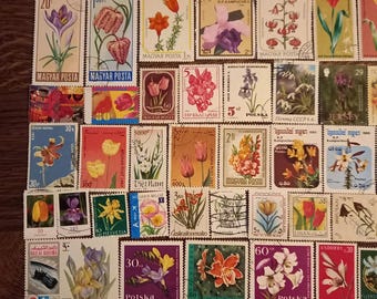 May include: A collection of vintage postage stamps featuring colorful floral illustrations. The stamps showcase various flowers, including tulips, orchids, and irises, with text in multiple languages and denominations.