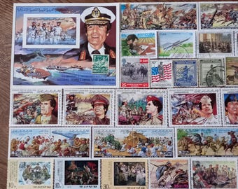 Może przedstawiać: Kolekcja znaczków pocztowych przedstawiających sceny historyczne i militarne, w tym duży znaczek z portretem Muammara Kaddafiego w czapce wojskowej oraz różne mniejsze znaczki przedstawiające żołnierzy, czołgi i flagi różnych narodów.