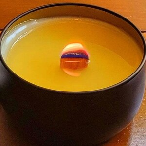 May include: A black candle jar with a yellow wax candle inside. The candle is lit and the flame is visible.