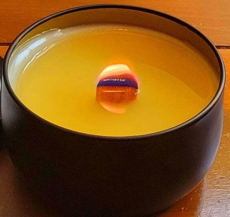 May include: A black candle jar with a yellow wax candle inside. The candle is lit and the flame is visible.
