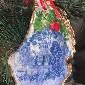 May include: A blue and white porcelain design with a gold trim, depicting a pagoda and a fence, is featured on a Christmas ornament made from an oyster shell.